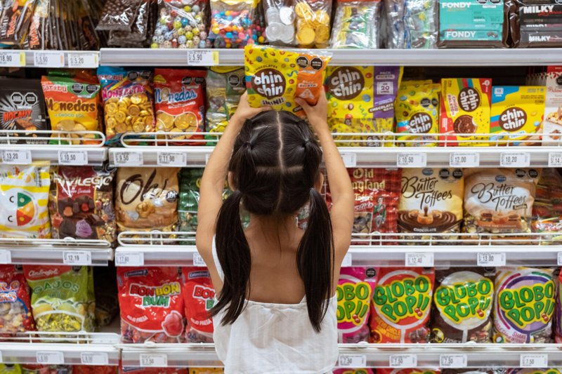Garota pega um pacote de doces em prateleira de supermercado