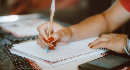 Mulher estudando e escrevendo em caderno em casa