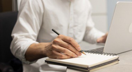 Close up empresário mão escrevendo conteúdo ou algo no notebook com o uso de laptop na mesa de madeira no escritório em casa para pessoas e conceito de estilo de vida