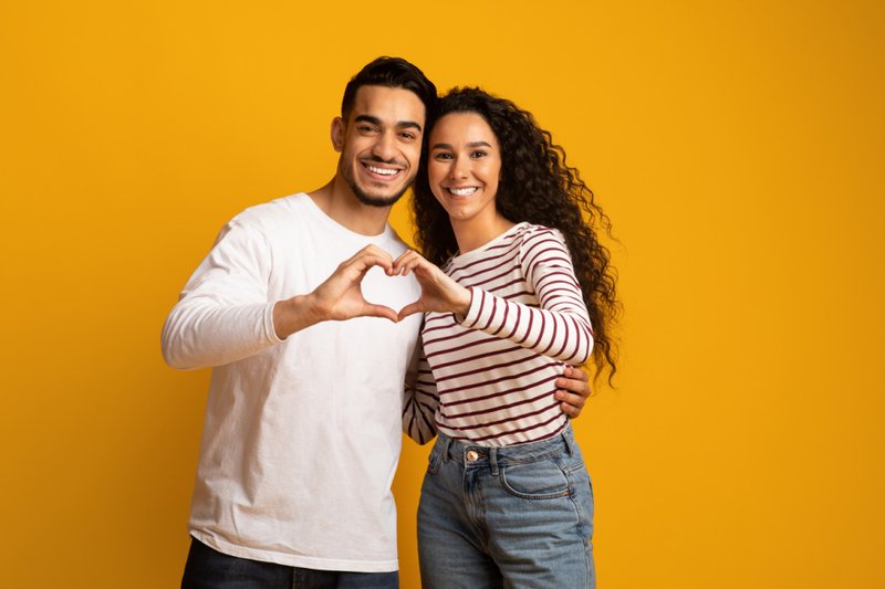 Imagem de casal romântico fazendo gesto de coração com as mãos juntas