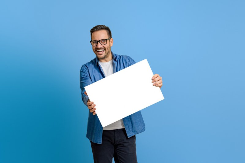 Imagem de um homem alegre mostrando o banner branco em branco enquanto está no fundo azul 