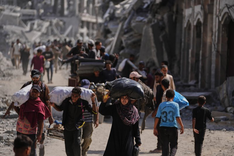 Palestinos deslocados com seus pertences passam por prédios destruídos enquanto retornam para suas casas em Khan Younis, no sul da Faixa de Gaza