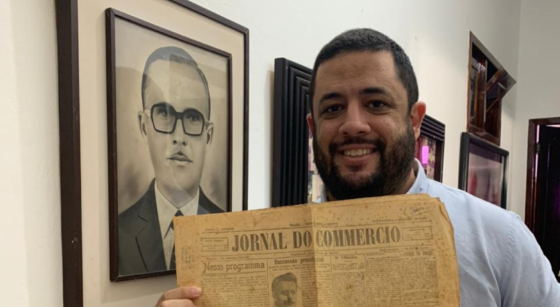 Ao lado da foto do av&ocirc;, o jornalista Lu&iacute;s Boaventura posa ao lado da primeira edi&ccedil;&atilde;o impressa do Jornal do Commercio
