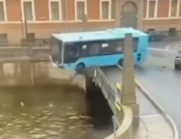 Ônibus azul rompendo a barreira de segurança de uma ponte e caindo em um rio