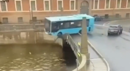 Ônibus azul rompendo a barreira de segurança de uma ponte e caindo em um rio