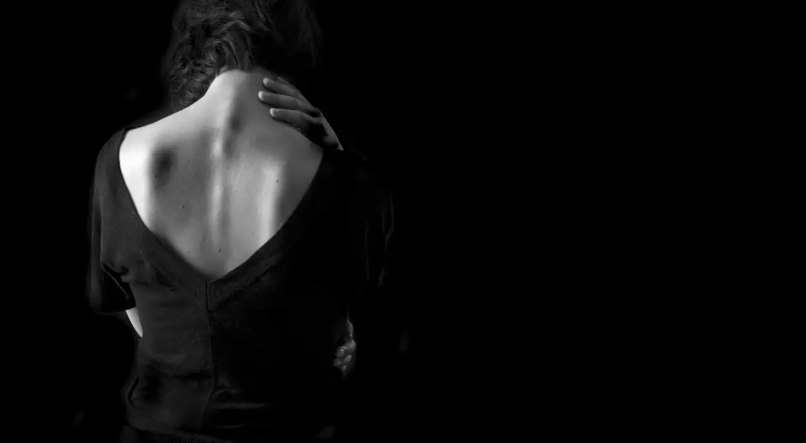Foto de mulher de costas no escuro em fundo preto para representar situação de violência sexual
