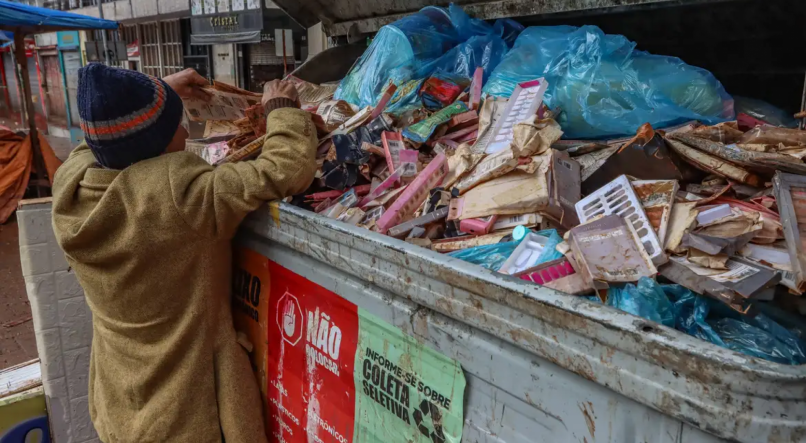 Homem em situação de rua vasculha caçamba de lixo