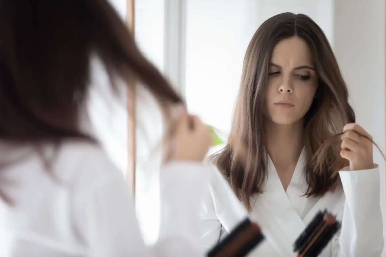 Imagem ilustrativa de mulher descontente com seu cabelo e se olhando no espelho