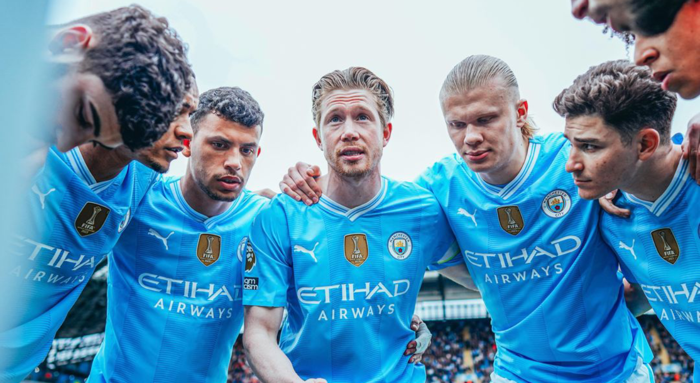 Imagem: jogadores do Manchester City abraçados em roda de conversa
