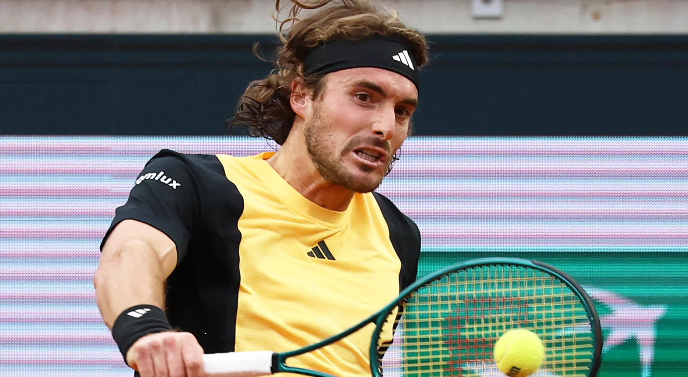 Imagem: Tsitsipas com camisa amarela e preta, segurando a raquete