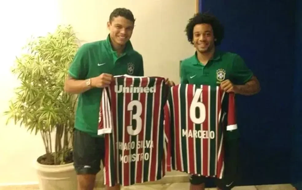 Imagem de Thiago Silva ao lado de Marcelo na Seleção Brasileira com uma camisa do Fluminense nas mãos