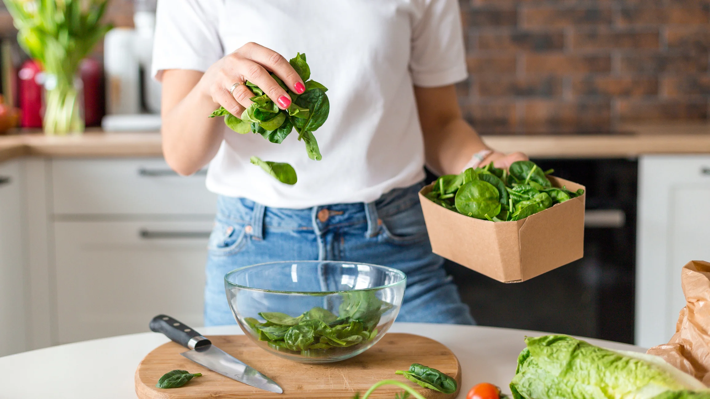 Imagem ilustrativa: mulher na coziha preparando salada com espinafre. 