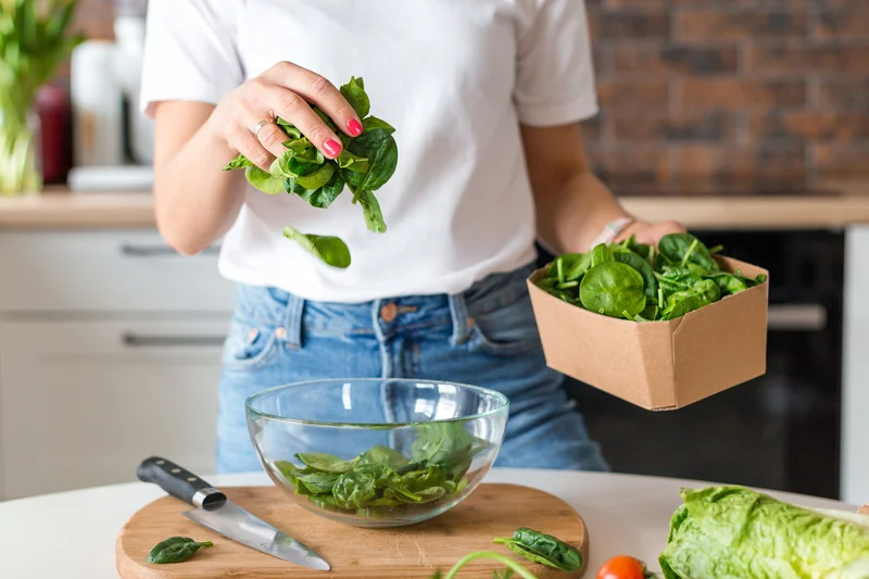 Imagem ilustrativa: mulher na coziha preparando salada com espinafre.