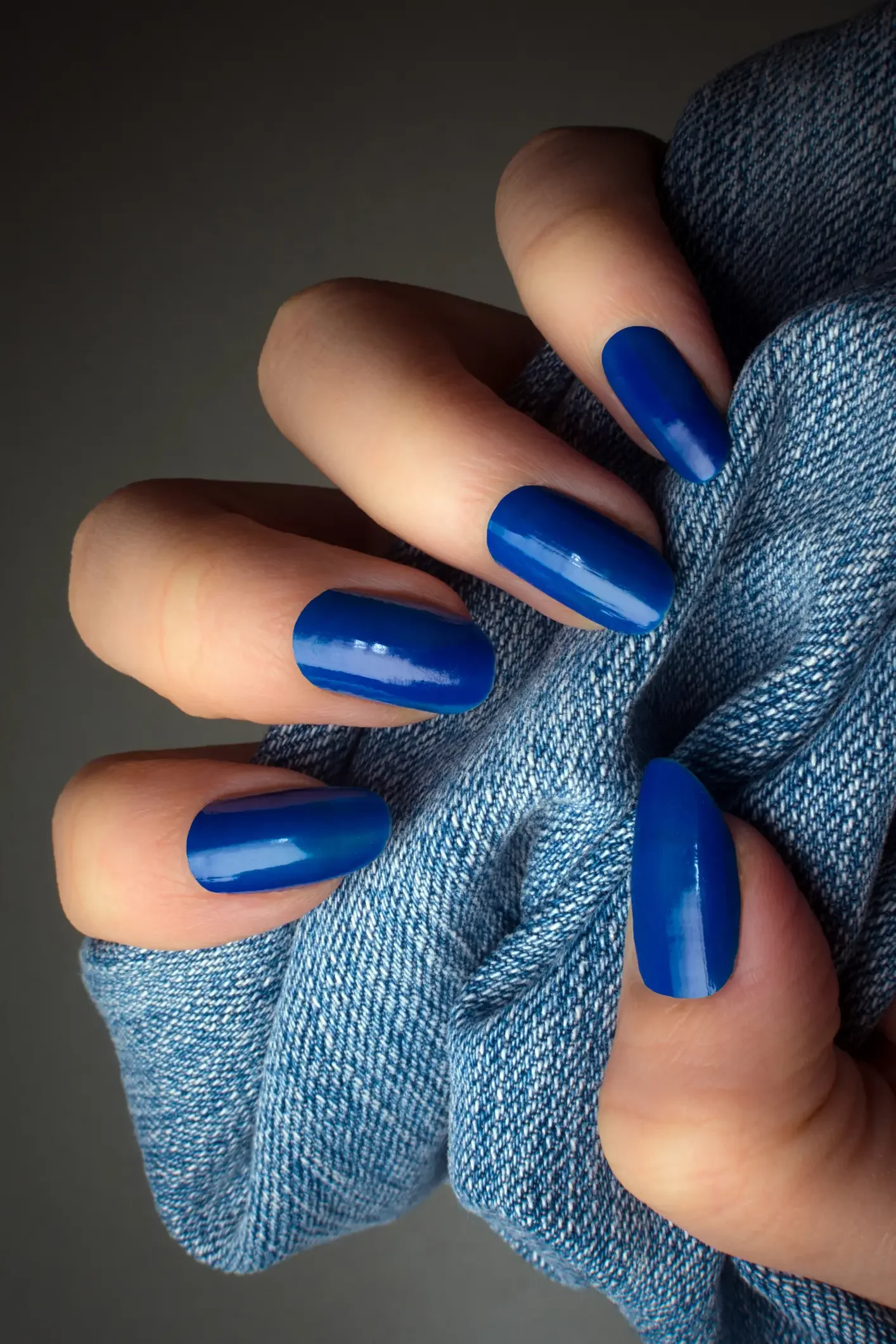 Imagem ilustrativa de unhas mão com unhas azuis segurando um tecido jeans