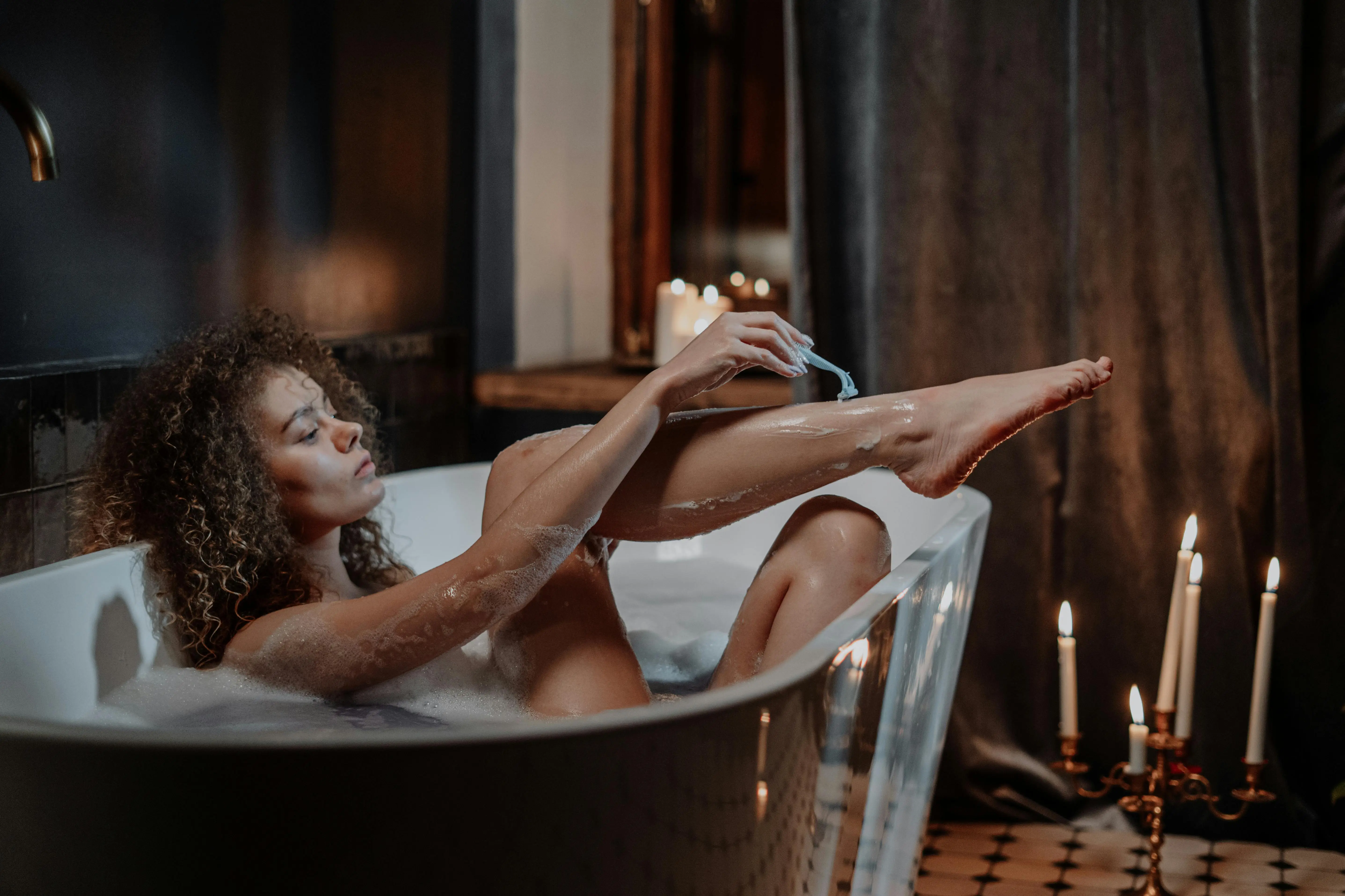 Imagem ilustrativa de mulher se depilando na banheira com lamina de barbear