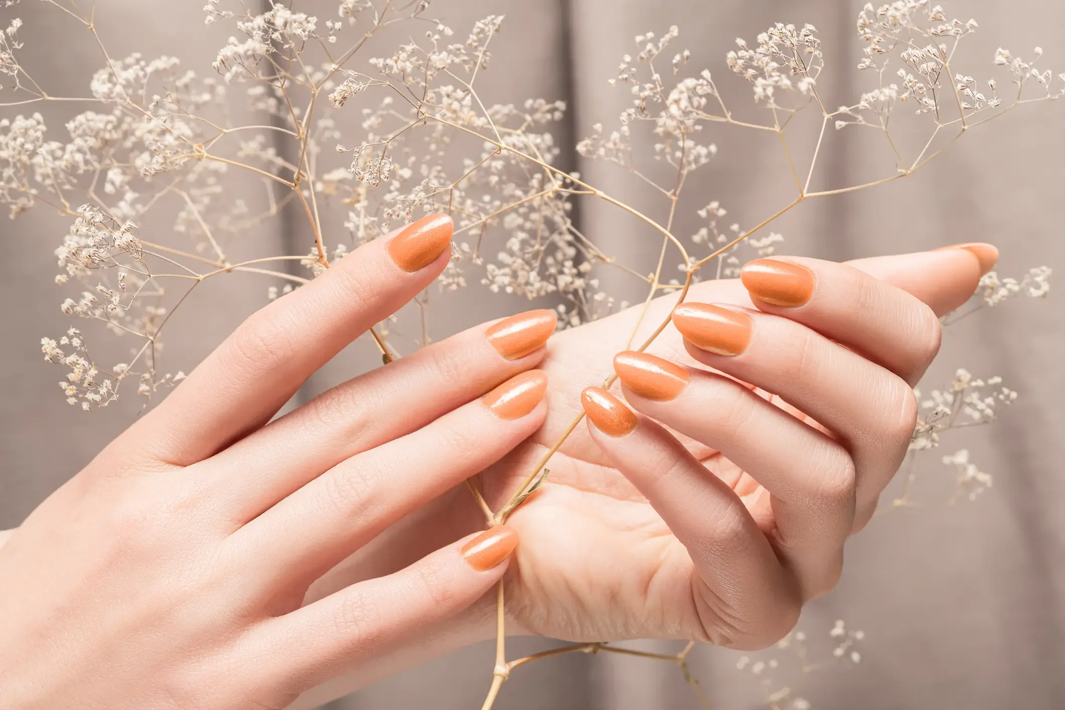 Imagem ilustrativa unhas laranjas segurando flores