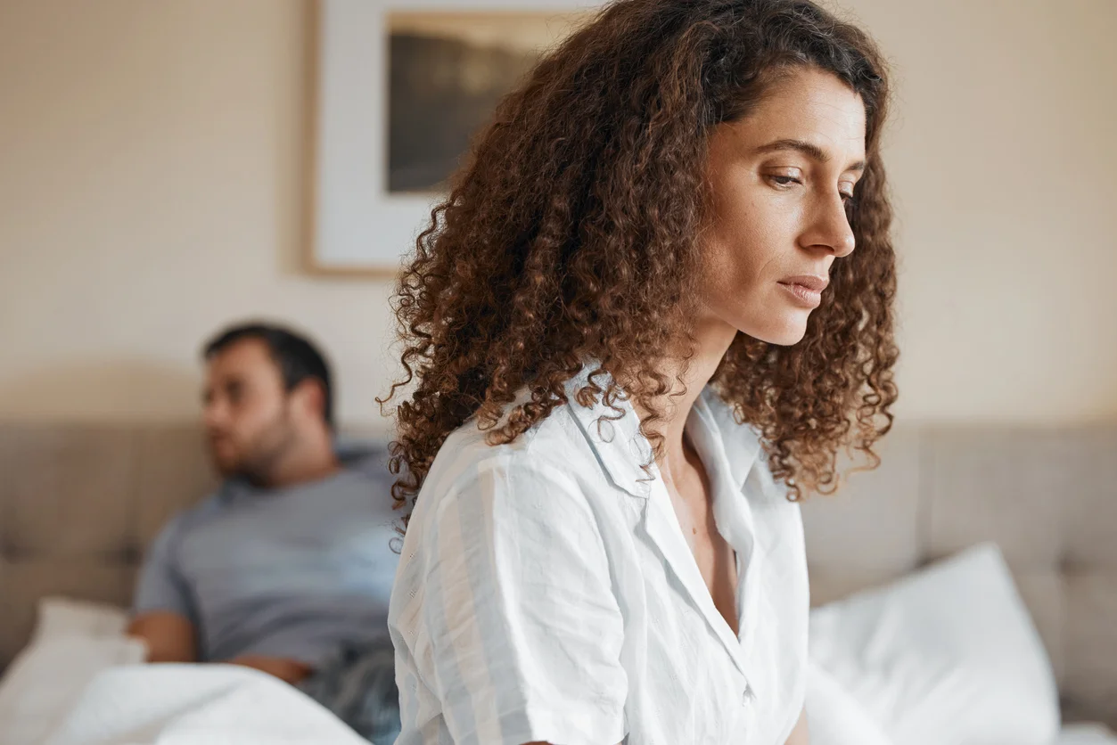 Imagem de uma mulher e um homem em uma cama, com express&otilde;es cansadas