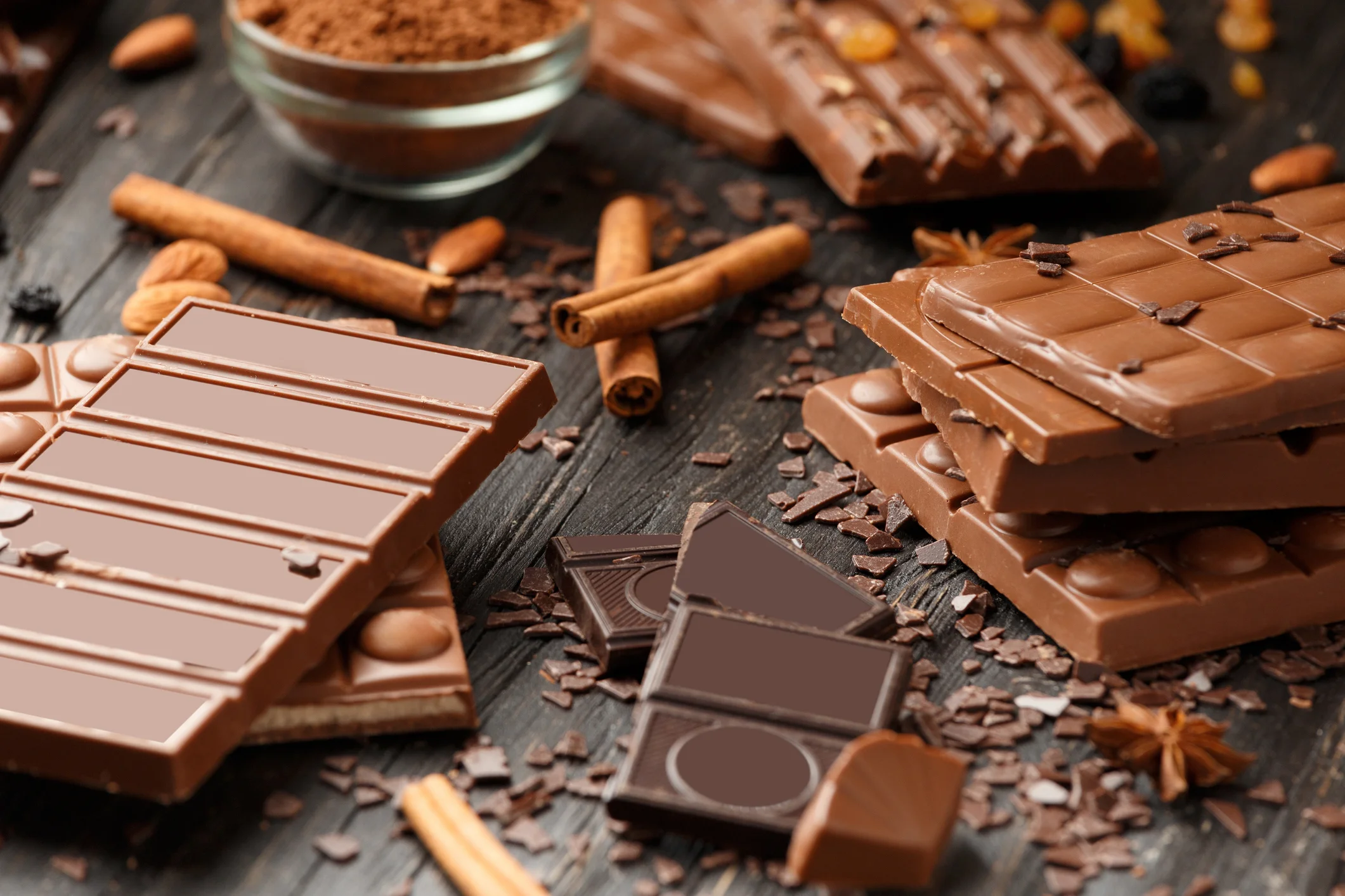 Barras de chocolate ao leite e doces em um fundo escuro.