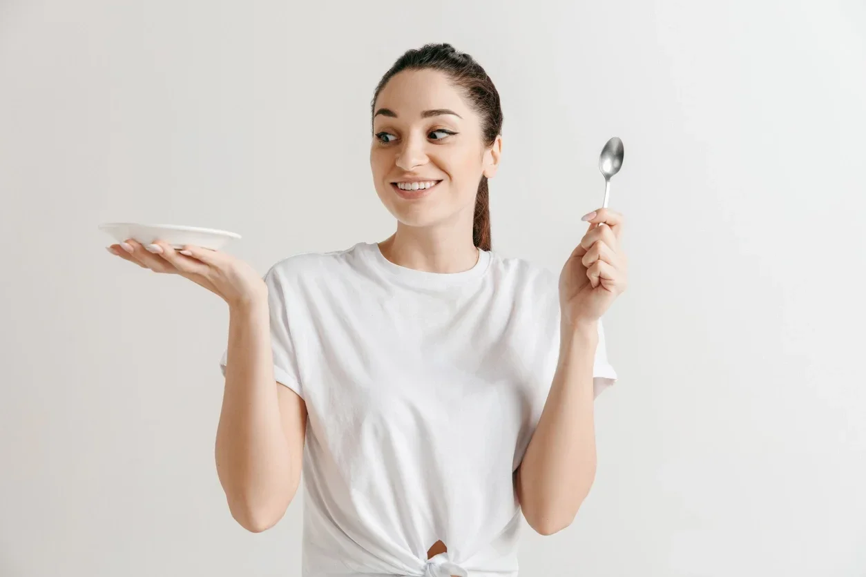 Dona de casa triguenha louca do divertimento novo com a colher isolada no fundo branco