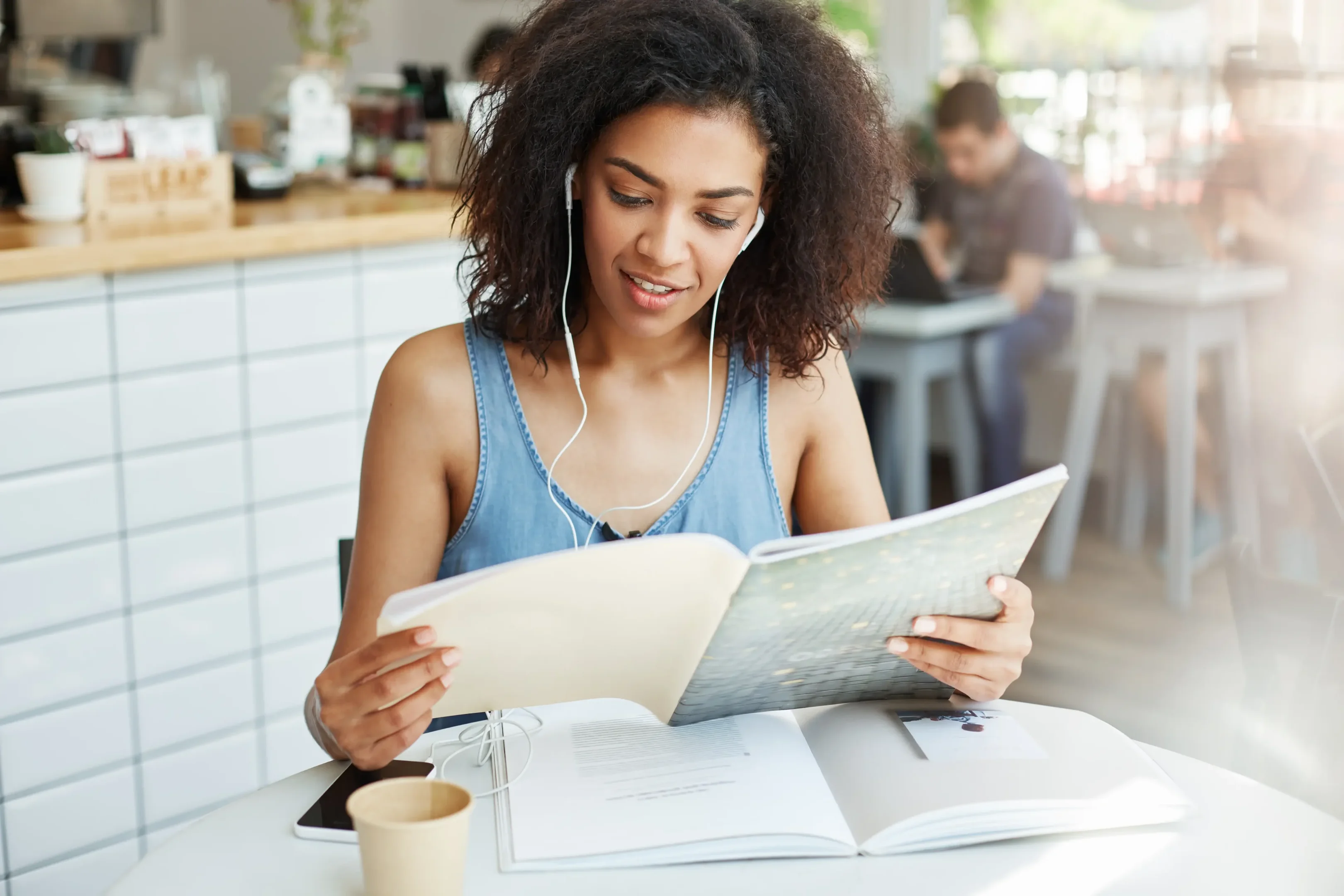 Imagem: jovem estudando por meio de fichas, com fones de ouvido em um café.