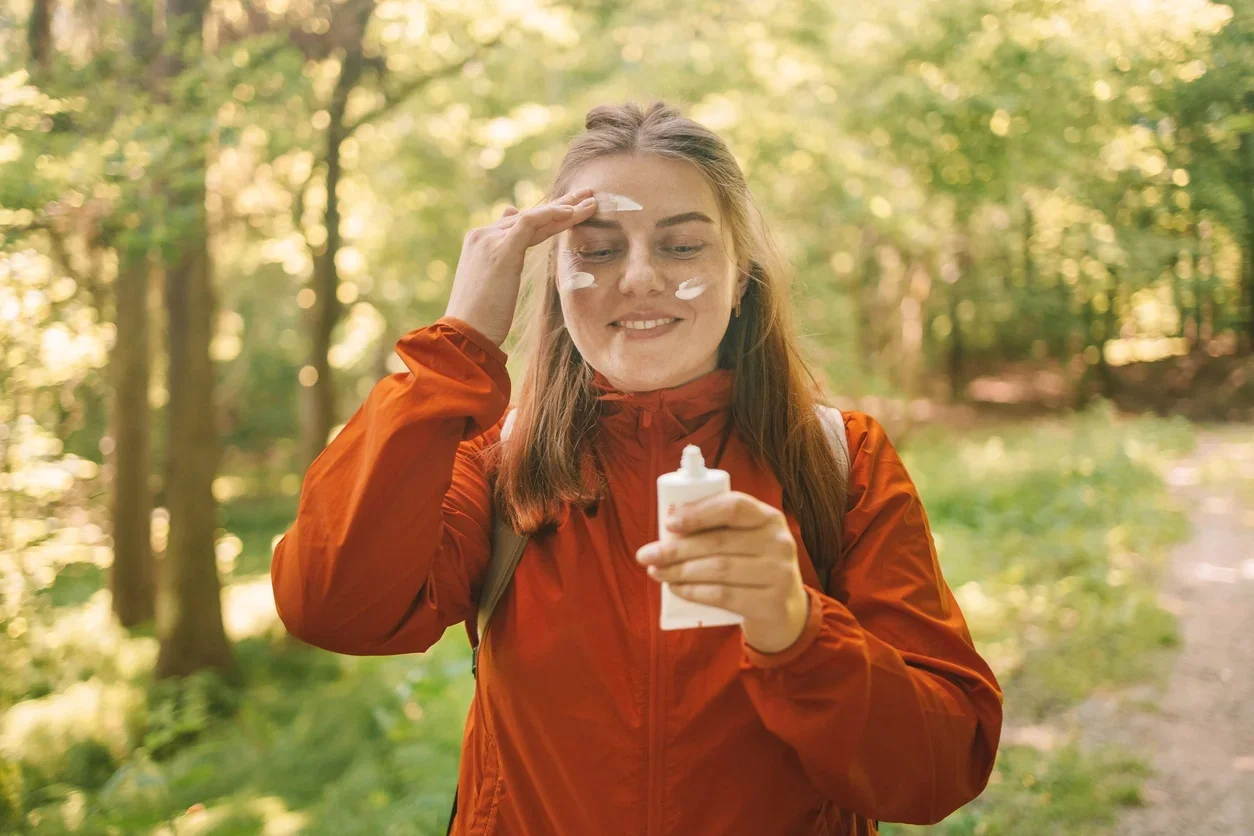 Mulher nova em uma roupa de esporte laranja aplicando protetor solar loção enquanto viaja nas montanhas